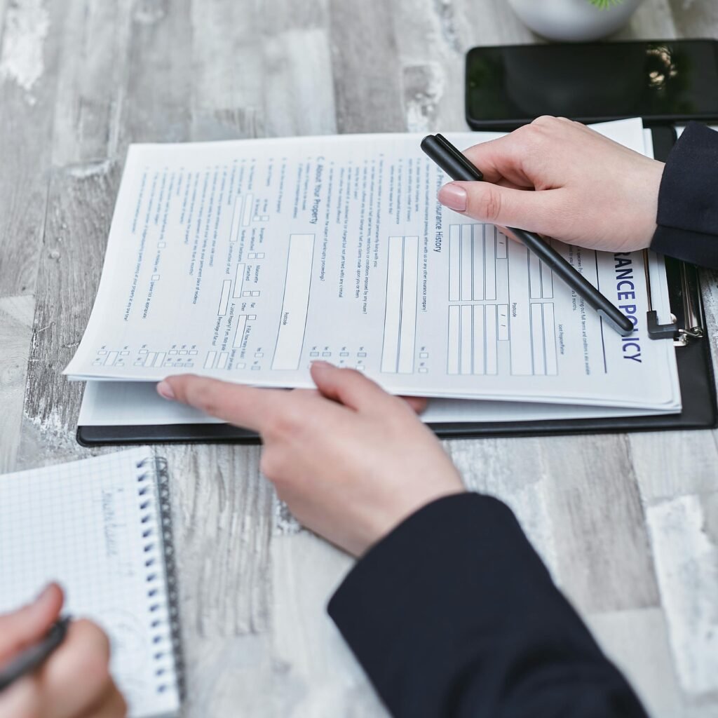Close-up of hands analyzing insurance policy paperwork with pen on table.